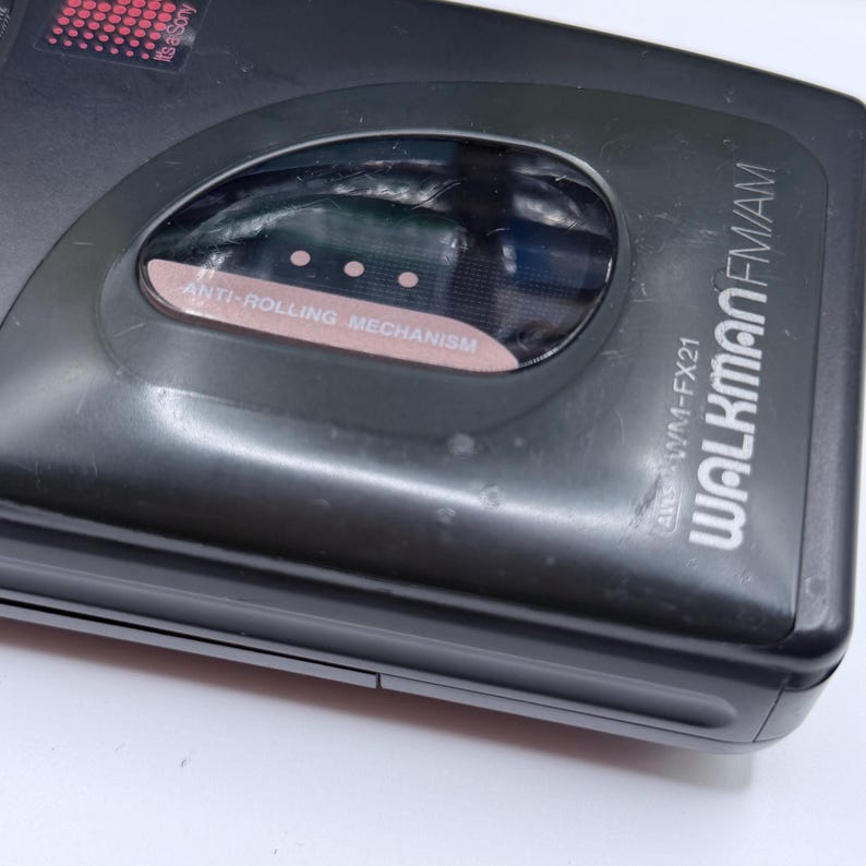 May include: A black Sony Walkman FM/AM radio cassette player. The device has a clear window with the words "ANTI-ROLLING MECHANISM" printed on it. The model number "WM-FX21" is visible.