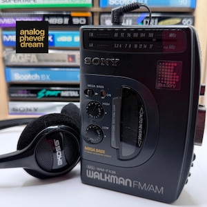 May include: A black Sony Walkman FM/AM radio with a pair of black headphones. The Walkman has a Mega Bass feature and a digital display. The text "analog phever dream" is in the upper left corner.