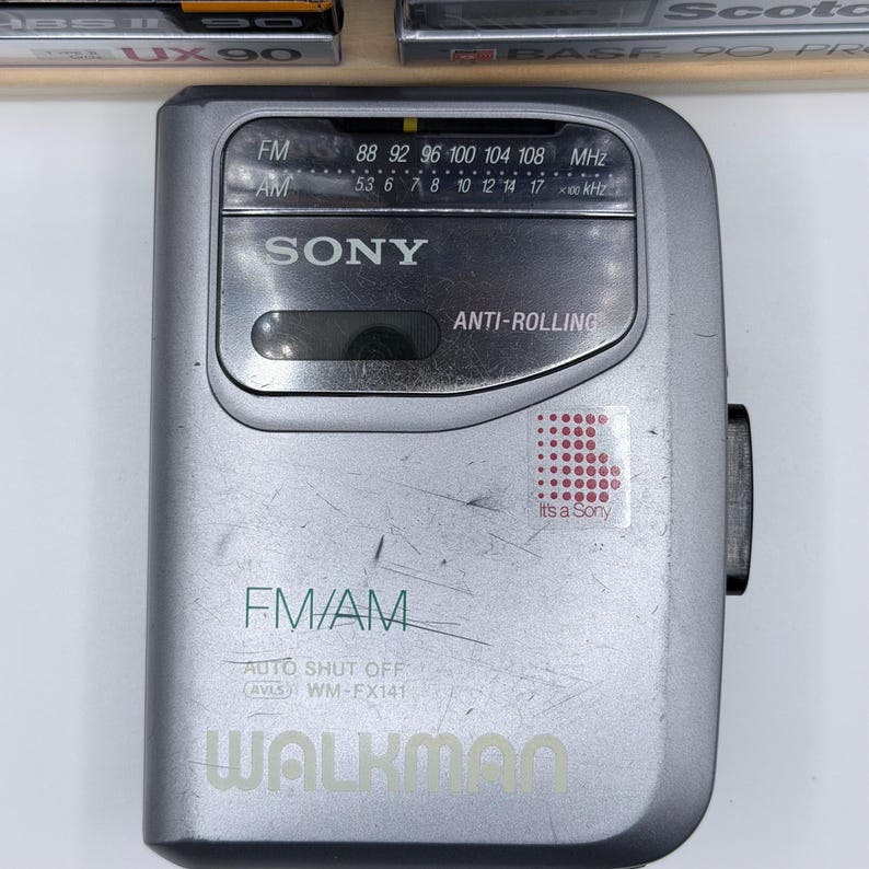 Peut inclure: Un lecteur de cassettes portable Sony Walkman argent&eacute; avec radio FM/AM. L'appareil comporte un cadran de r&eacute;glage, un &eacute;cran et le texte "WALKMAN" en bas. La radio porte l'inscription "It's a Sony" sur un autocollant.