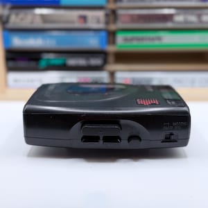 May include: A black portable CD player with buttons for play, stop, and other functions. The device has a digital display and a headphone jack. Cassette tapes are visible in the background.