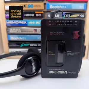 May include: A black Sony Walkman FM/AM radio cassette player model WM-FX30 with an anti-rolling mechanism and auto reverse feature, paired with black Koss headphones. The device features a radio frequency tuner display and a cassette compartment window.