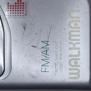 Peut inclure: Un lecteur de cassettes portable Sony Walkman WM-FX141 argent&eacute;. L'appareil porte l'inscription "WALKMAN" en vert clair, avec "FM/AM" et "AUTO SHUT OFF" &eacute;galement visibles. Un autocollant rouge avec le texte "It's a Sony" est dans le coin sup&eacute;rieur gauche.