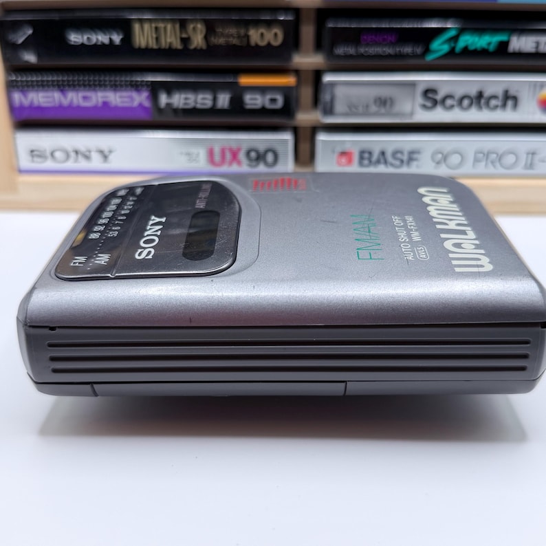 Peut inclure: Un lecteur de cassettes radio FM/AM Sony Walkman argent&eacute;. L'appareil a une forme rectangulaire avec un panneau avant gris fonc&eacute;. Le mot "SONY" est imprim&eacute; sur le devant, ainsi que le mot "WALKMAN". La radio est entour&eacute;e de cassettes audio.