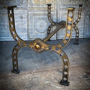May include: Antique bronze-colored table legs with a decorative, openwork design. The legs are made of metal and feature a curved shape with circular cutouts and the text "Drake Casting Co."
