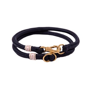 May include: A navy blue rope dog collar with a gold metal clasp and a small gold ring. The collar has the text "The Pawsitive" printed on it.
