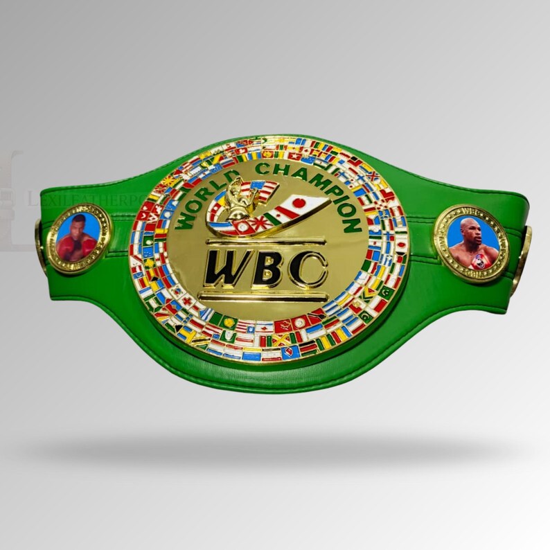 May include: A green leather boxing championship belt with a gold center plate. The center plate has the text "WBC" and "WORLD CHAMPION" with flags around the edge. Two circular medallions with boxer portraits are on each side.