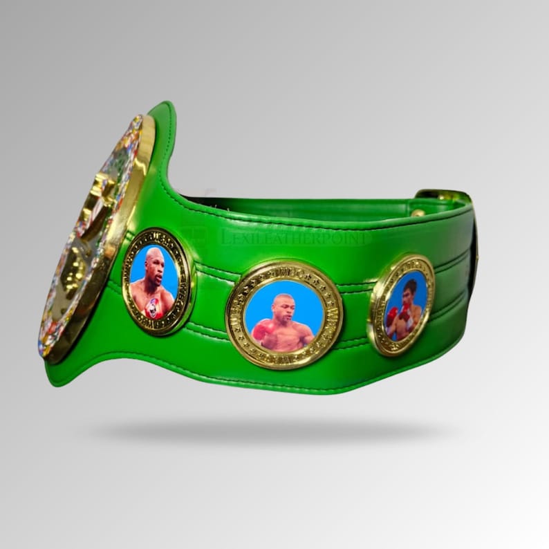 May include: A green boxing championship belt with gold accents and three circular medallions featuring images of boxers. The belt has a large gold emblem on the left side and a gold buckle.