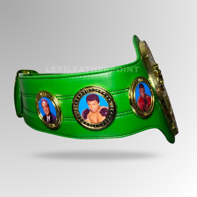 May include: A green boxing championship belt with gold accents. The belt features three circular medallions with portraits of boxers. The belt is made of a shiny, smooth material and has a curved design.