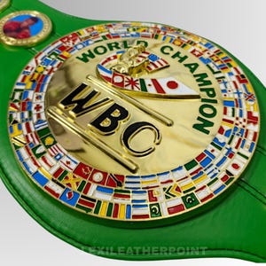May include: A green leather boxing championship belt with a gold center plate. The plate features the text "WORLD CHAMPION" and "WBC", surrounded by flags of various nations. A small image of a boxer is on the side.