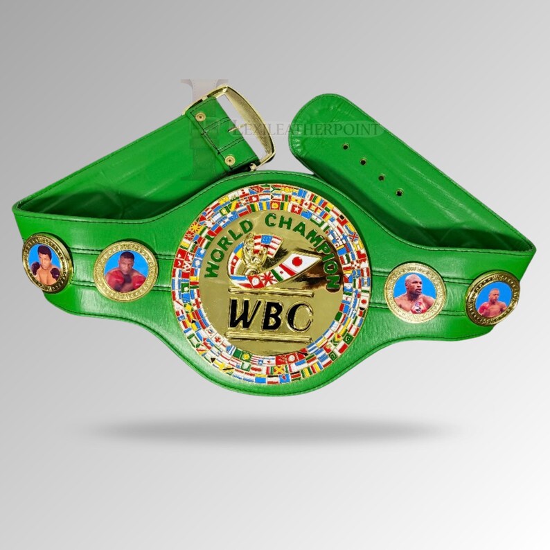 May include: A green leather World Boxing Council (WBC) championship belt. The belt features a gold center plate with the WBC logo and the words "World Champion." It has portraits of boxers on the sides and a gold buckle.