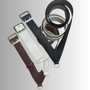 May include: An assortment of leather belts in various colors, including brown, white, and black. Each belt features a metal buckle and a D-ring. Several rolled belts are also visible in the background.
