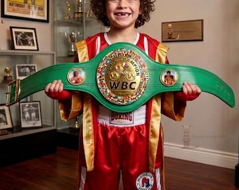 May include: A green WBC world champion boxing belt with gold accents and circular portraits, worn with a red and gold satin boxing robe and matching red and white boxing shorts featuring a circular logo and the text BOXING on the waistband.