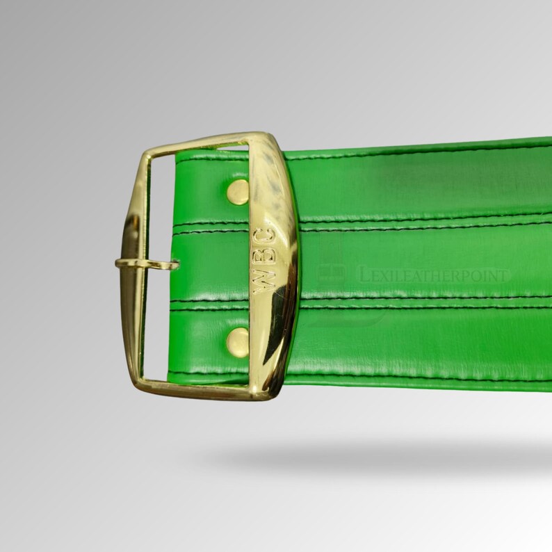 May include: A close-up of a green leather belt with a gold buckle. The buckle has the letters "WBC" engraved on it. The belt is stitched with black thread and has a rectangular shape. The image is well-lit and the colors are vibrant.