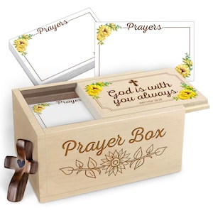 Op de afbeelding: Een houten gebedsdoos met een zonnebloem- en wijnstokontwerp, met notitiekaarten met bloemaccenten en het woord "Prayers". Het deksel van de doos heeft de tekst "God is with you always". Aan de zijkant staat een houten kruis.