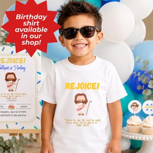 K&ouml;nnte beinhalten: Ein wei&szlig;es T-Shirt mit dem Wort "REJOICE!" in Gelb, mit einer Cartoon-Illustration von Jesus. Das Shirt enth&auml;lt auch den Text "Dies ist der Tag, den der HERR gemacht hat; lasst uns jubeln und uns an ihm freuen" und "Psalm 118,24".