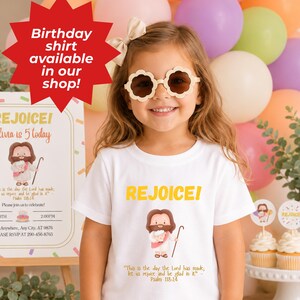 Op de afbeelding: Een jong meisje draagt een wit t-shirt met het woord "REJOICE!" in het geel, samen met een cartoonillustratie van Jezus. Het shirt bevat ook een bijbelvers. Het meisje draagt bloemvormige zonnebrillen en lacht. Ballonnen zijn op de achtergrond.