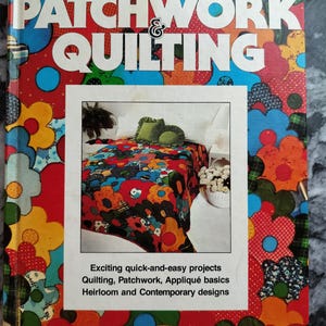 Peut inclure: Couverture de livre vintage "Better Homes and Gardens Patchwork & Quilting". La couverture présente un motif floral vibrant en rouge, bleu, jaune et vert. Le titre est en grandes lettres blanches sur fond rouge et bleu. La couverture du livre comprend également une photo d'une courtepointe.