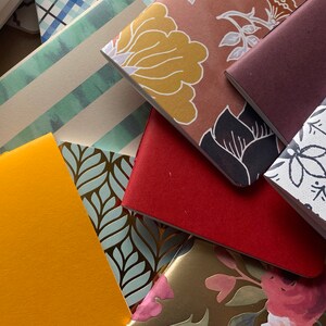 Puede incluir: Una pila de peque&ntilde;os cuadernos coloridos con varias cubiertas estampadas. Las cubiertas incluyen dise&ntilde;os florales, patrones geom&eacute;tricos y colores s&oacute;lidos.