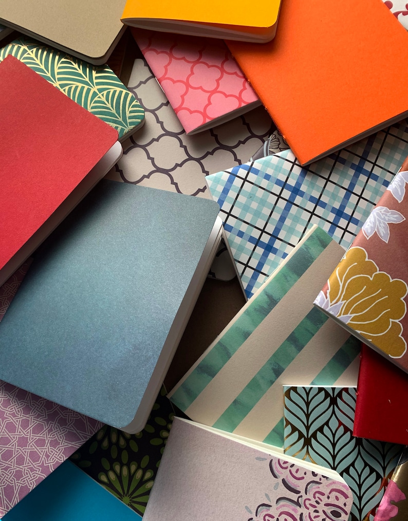 Puede incluir: Una colecci&oacute;n de peque&ntilde;os cuadernos coloridos con varios patrones y dise&ntilde;os. Los cuadernos est&aacute;n apilados y dispuestos en un orden aleatorio, creando una composici&oacute;n visualmente atractiva y texturizada.