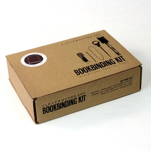 May include: A brown cardboard box with the text "CLEVERHANDS.COM BOOKBINDING KIT instructions Supplies Tools" printed on the front. The box contains a bookbinding kit with tools and supplies.