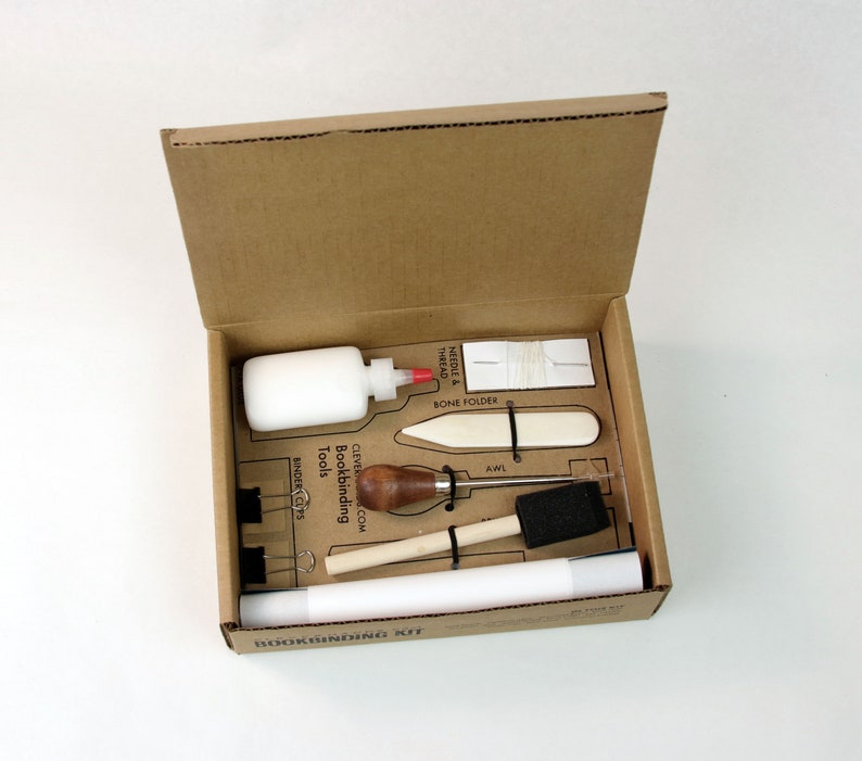 May include: A bookbinding kit in a cardboard box with tools including a bone folder, awl, binder clips, needle and thread, glue, and a wooden tool. The box has the text "Bookbinding Kit" printed on it.