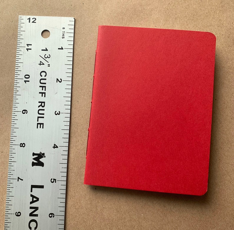 Puede incluir: Un peque&ntilde;o cuaderno de tapa dura de color rojo con una cubierta lisa. El cuaderno mide aproximadamente 10 cm de alto y 7,5 cm de ancho.