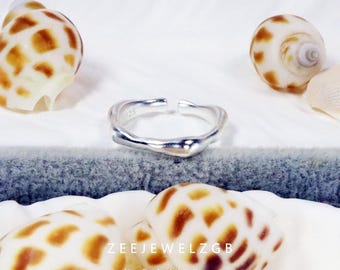 May include: A silver ring with an irregular, flowing shape, displayed with seashells. The ring has an open design and a shiny finish. The image also includes the text "ZEEJEWELZGB Handcrafted Jewellery".