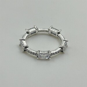 May include: A silver ring featuring rectangular and round clear gemstones. The ring is engraved with the word "PANDORA" on the inside. The ring is set against a light grey background.