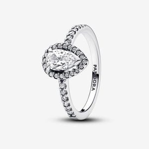 Op de afbeelding: Een zilverkleurige ring met een centrale peervormige heldere steen omringd door een halo van kleinere ronde heldere steentjes. De ringband is versierd met een rij kleine ronde steentjes en heeft de inscriptie PANDORA aan de binnenzijde.