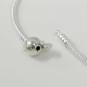 May include: A silver bracelet with a Mickey Mouse-shaped clasp. The clasp is detailed with the word "Disney" and a small black circle. The bracelet is unclasped, showing the two ends of the chain.