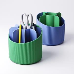 May include: Two desk organizers in green and blue. The green organizer holds a yellow pencil, scissors, and pens. The blue organizer has a green insert. Both organizers have a ribbed texture and are on a white background.