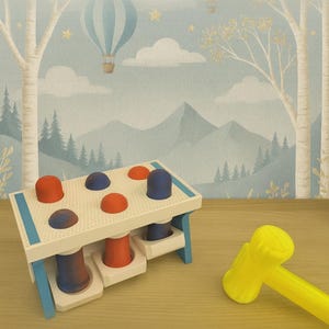 以下が含まれることがあります： 白いフレーム、青いアクセント、格子状のトップを備えた木製のおもちゃ。赤と青のペグがあり、黄色のハンマーが付属しています。背景には、熱気球と木々のある気まぐれな風景が描かれています。