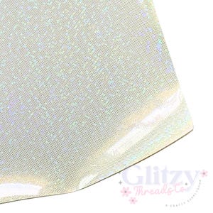 Puede incluir: Una lámina de tela iridiscente con un patrón de puntos. La tela tiene un brillo nacarado, que refleja un espectro de colores. El logotipo de Glitzy Threads Co. es visible en la esquina inferior derecha. Este material es adecuado para proyectos de manualidades y costura.