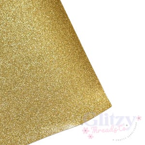 May include: Close-up of a sheet of gold glitter paper. The paper is covered in small, sparkling particles, creating a textured surface. The corner of the paper is visible, with a white background. The Glitzy Threads Co. logo is in the bottom right corner.