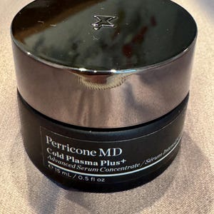 May include: A black jar of Perricone MD Cold Plasma Plus+ Advanced Serum Concentrate. The jar has a silver lid with a logo. The label indicates a volume of 15 mL / 0.5 fl oz.