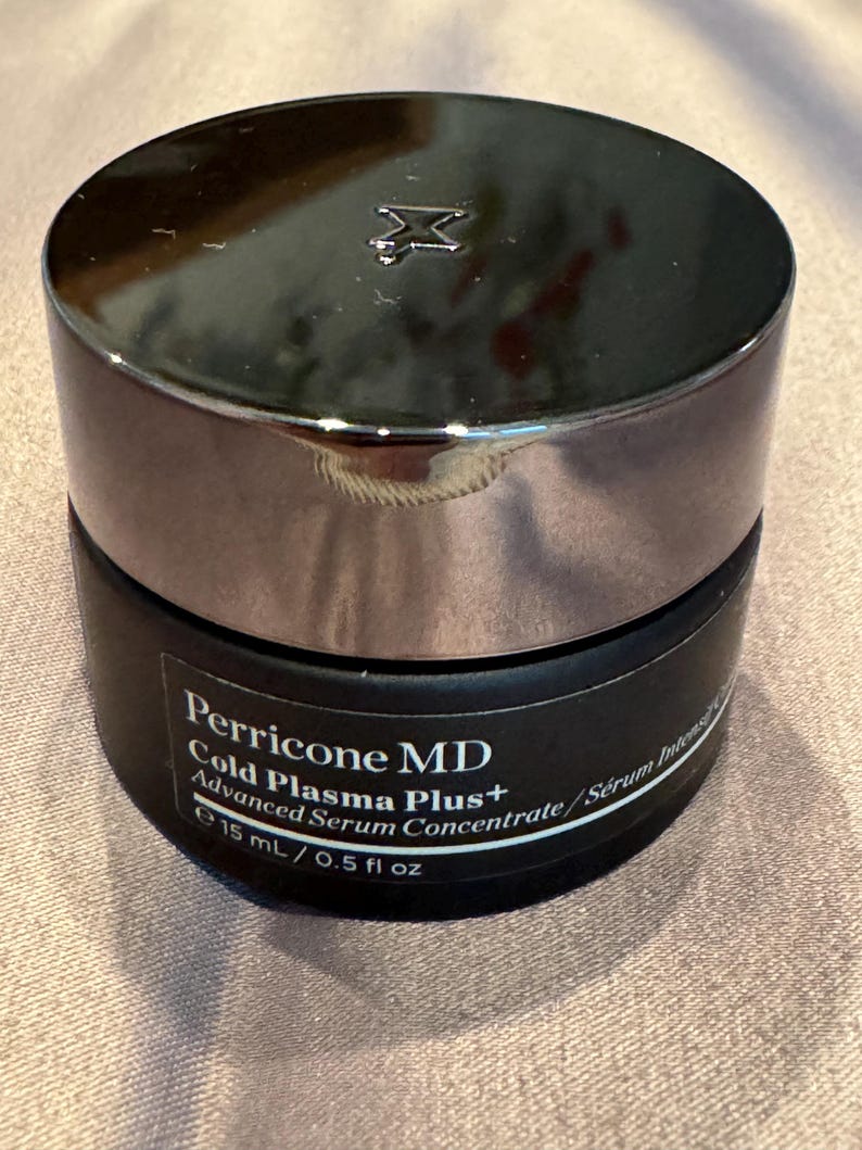 May include: A black jar of Perricone MD Cold Plasma Plus+ Advanced Serum Concentrate. The jar has a silver lid with a logo. The label indicates a volume of 15 mL / 0.5 fl oz.