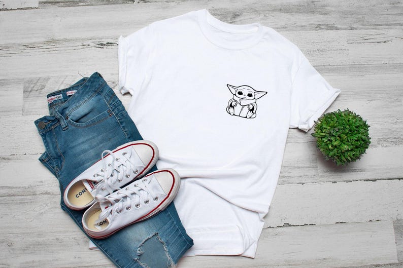 May include: White t-shirt with a black and white graphic of a cartoon character. The shirt is paired with blue jeans and white sneakers with red accents. A small green plant is also in the image.