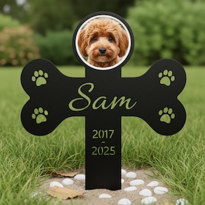 May include: A black metal pet memorial stake in a bone shape, featuring a photo of a brown dog. The name "Sam" is inscribed in green script, along with the years 2017-2025. Green paw prints decorate the bone ends.