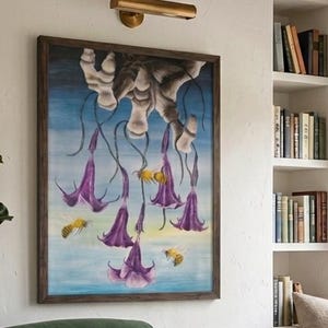 Può includere: Un accogliente angolo lettura con un dipinto floreale incorniciato con fiori viola e api. Una poltrona in velluto verde con una coperta e un libro aperto si trova su un tappeto fantasia. Un tavolino in legno contiene libri e una tazza, con una pianta in vaso e un gatto.
