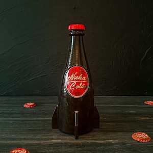 May include: A brown bottle-shaped decorative item with a red cap and the words "Nuka Cola" in a red oval. The bottle has fins and is surrounded by red bottle caps. The background is dark.