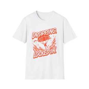 May include: White t-shirt featuring a red graphic of a parachutist. The words "DROPPING" and "LOCKED IN" are printed in red, with a stylized design around the parachute. A casual, comfortable tee.