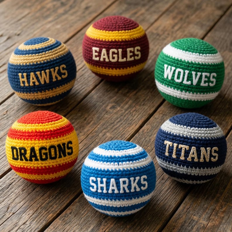 K&ouml;nnte beinhalten: Sechs kugelf&ouml;rmige H&auml;kelb&auml;lle mit horizontalen Streifen in verschiedenen Farben. Jeder Ball zeigt einen in Gro&szlig;buchstaben gestickten Teamnamen: HAWKS, EAGLES, WOLVES, DRAGONS, SHARKS und TITANS. Die Garnstruktur ist auf jedem Objekt sichtbar.