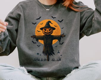 Könnte beinhalten: Ein dunkelgraues Sweatshirt mit einem Halloween-Motiv. Die Grafik zeigt eine Vogelscheuche mit einem Kürbiskopf, einem schwarzen Hut und ausgestreckten Armen, vor einem vollen orangefarbenen Mond und umgeben von Fledermäusen.