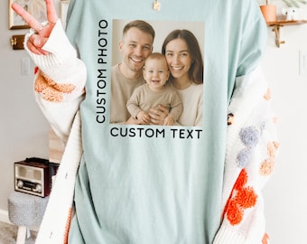 Könnte beinhalten: Hellblaues T-Shirt mit einem Familienfoto und dem Text "CUSTOM PHOTO" und "CUSTOM TEXT". Das Foto zeigt eine lächelnde dreiköpfige Familie. Das Shirt hat eine lockere Passform.