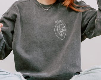 Könnte beinhalten: Dunkelgraues Sweatshirt mit einem weißen anatomischen Herzdesign auf der Brust. Das Sweatshirt hat einen Rundhalsausschnitt und lange Ärmel. Das Wort "PEPPER" ist unten rechts im Bild weiß gedruckt.