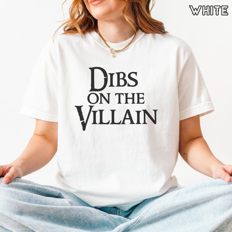 K&ouml;nnte beinhalten: Wei&szlig;es T-Shirt mit dem schwarzen Aufdruck "Dibs on the Villain". Das T-Shirt hat kurze &Auml;rmel und einen Rundhalsausschnitt. Das Wort "WHITE" ist in der oberen rechten Ecke aufgedruckt.