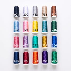 Peut inclure: Une collection de vingt bobines de fil &agrave; broder dispos&eacute;es en une grille de quatre par cinq. Chaque bobine pr&eacute;sente une couleur unie distincte, incluant des nuances de bleu, rose, jaune, vert, violet, orange, gris, marron et noir, avec des &eacute;tiquettes num&eacute;riques.