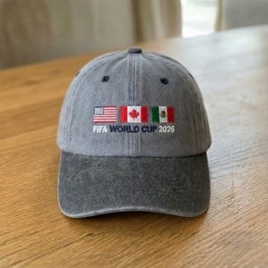 May include: Gray baseball cap with the text "FIFA WORLD CUP 2026" embroidered below the flags of the United States, Canada, and Mexico. The cap is made of a soft material and has a curved brim.