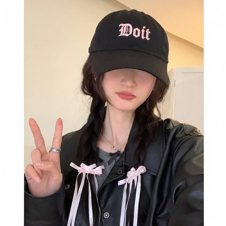 May include: Black baseball cap with the word "Doit" embroidered in pink script. The cap is worn by a person wearing a black leather jacket and a gray shirt. The person is also wearing a silver ring and necklace.