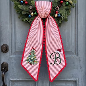 May include: A decorative fabric door hanger featuring red and white vertical stripes with scalloped red edges. One side displays an embroidered green Christmas tree with colorful ornaments, while the other side shows a large dark green letter B with a Santa hat.